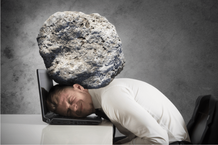 man with head on laptop and burdened by rock