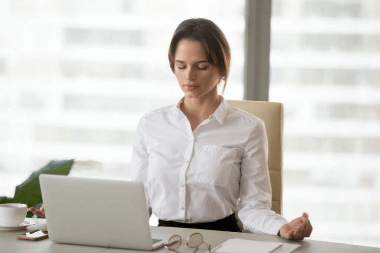 woman doing meditation on office desk in front of laptop