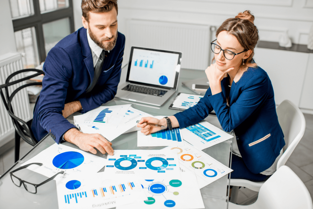 2 people discussing with charts and analysis papers on desk