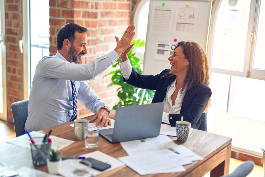 Client and customer sitting on desk with laptop, giving hifive and looks happy