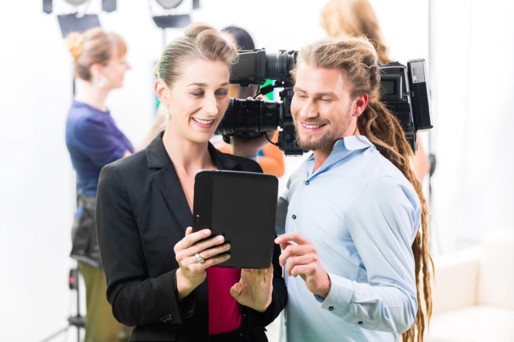 a man holding a cinema camera with a lady showing something to him on her ipad device