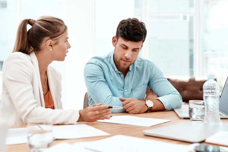 Two people on desk consulting with papers on table.