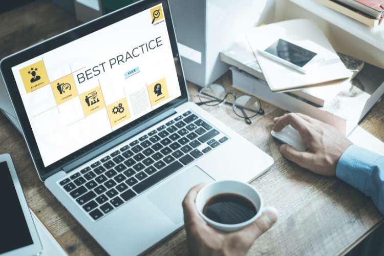 A person holds a coffee cup while using a laptop displaying a "Best Practice" presentation.