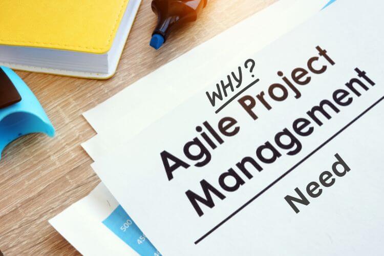 A paper on a wooden desk titled "Agile Project Management" with "WHY?" written above.